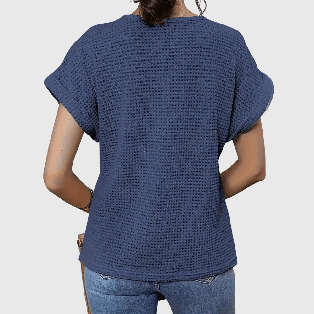 Isabel y Miguel Madrid Perla™ elegant Ibiza-style blouse with flowing fabric and intricate embroidery, displayed on a hanger.